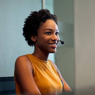 A beautiful young female receptionist sitting in front of a computer, wearing a headset and smiling.