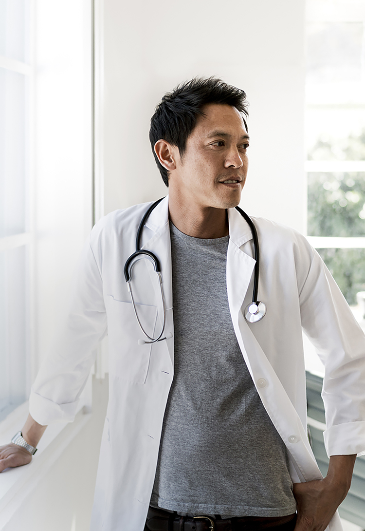 A photo of confident doctor standing by window in office